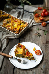Piece of freshly baked savory pie (quiche) with green beans, peas, bell pepper, cherry tomatoes and cheese  on white plate on rustic wooden table.
