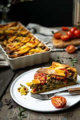Piece of freshly baked savory pie (quiche) with green beans, peas, bell pepper, cherry tomatoes and cheese  on white plate on rustic wooden table.