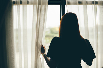 Thoughtful woman standing with looking at window, sad depressed teenager spending time alone at...