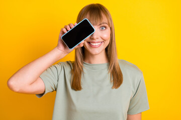 Close-up portrait of lovely cheerful girl demonstrating gadget having fun closing eye isolated over bright yellow color background