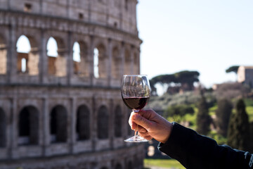 glass of red wine in a man's hand on the background of the Colosseum