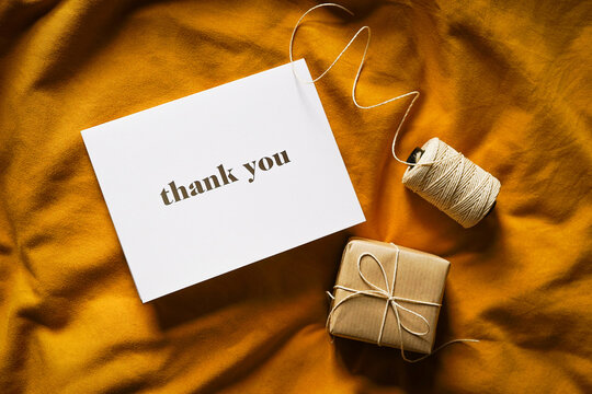 Thank you card on yellow fabric background with a small gift and twine. Elegant feminine composition. Special thank you note.