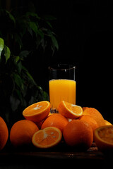 Orange juice in a glass. Ripe oranges on a dark background.