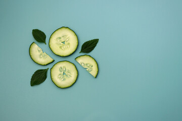Circles and semicircles of a cucumber with green mint leaves on a light blue background. Fresh summer background. 
