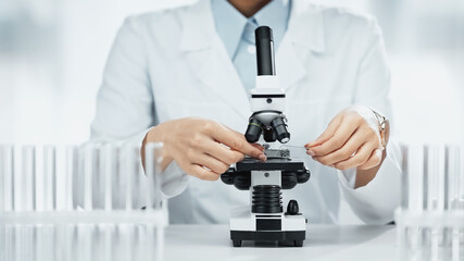cropped view of african american scientist holding glass with sample near microscope in lab