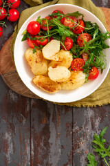 Baked potatoes and salad in a plate on a dark wooden background top view. Tasty rustic lunch or dinner, vegan food. Baked potatoes with tomatoes, arugula, and spices. Copy space for text