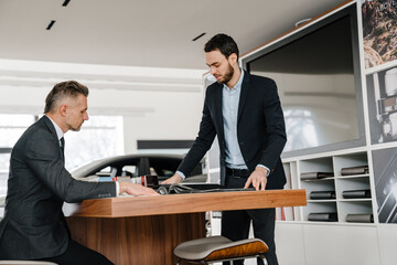 Salesman and client sitting at the desk in car dealeship