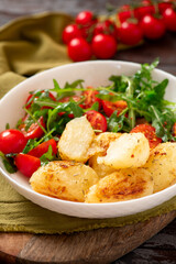 Baked potatoes and salad in a plate on a dark wooden background. Tasty rustic lunch or dinner, vegan food. Baked potatoes with tomatoes, arugula, and spices.