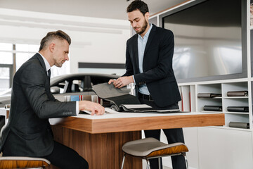 Salesman and client sitting at the desk in car dealeship
