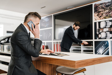 Salesman and client sitting at the desk in car dealeship