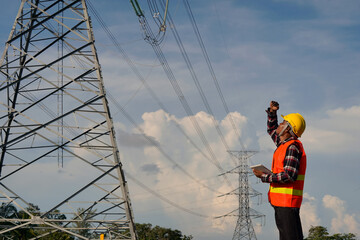 A male engineer uses a laptop and is inspecting the construction work. A large electric power pole in front of the construction site.