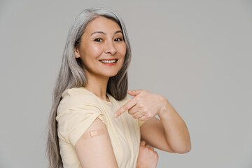 Smiling white-haired woman pointing finger at her bandage