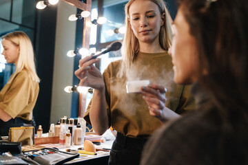 Blonde young woman doing makeup for her client in beauty salon