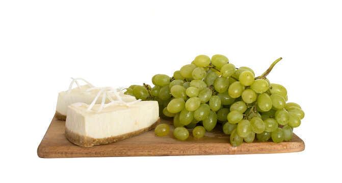 Two pieces of cheesecake decorated with white chocolate and a bunch of grapes on a wooden board for serving. Isolated on white background