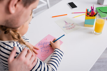 partial view of child drawing happy womens day card near father on blurred foreground