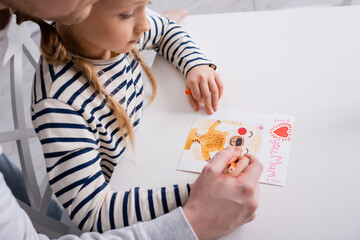girl drawing greeting card with i love you mum lettering  near father on blurred foreground