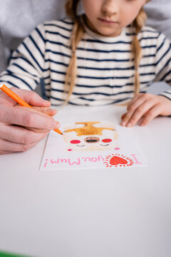 cropped view of father helping daughter drawing greeting card with i love you mum lettering, blurred background