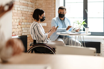Multiracial two colleagues in face mask using smartphone while working
