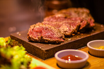 freshly cut piece of steak on the hot stone with sauces and side salad