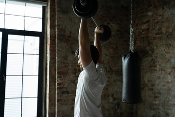 Muscular fitness man lifting barbell above his head in modern gym. Functional training