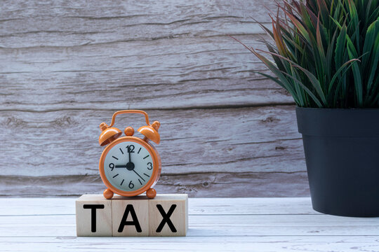 Tax text on wooden block cube with alarm clock and potted plant