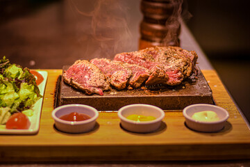 freshly cut piece of steak on the hot stone with sauces and side salad
