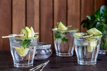 Drei Gläser erfrischendes Wasser mit Gurke, Ananas und Pfefferminze vor Holzwand