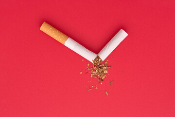 A broken cigarette with scattered tobacco. Quit smoking concept. No tobacco day. Red background,...