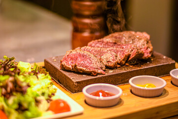freshly cut piece of steak on the hot stone with sauces and side salad
