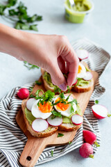 Woman seasoning avocado and egg toasts for breakfast with herbs, top view