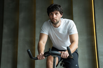 Plakat Young fitness man exercising his legs cardio training on bicycle in gym. Man working out on spinning bikes in gym