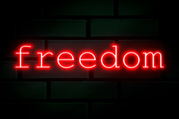 Red neon inscription - freedom on a green brick wall.