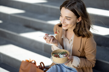 Pretty woman have outdoor lunch near office building while sitting on the stairs and smile. Healthy...