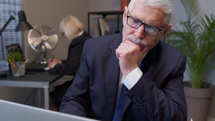 Thoughtful senior professional businessman grandfather director working on laptop inside office pondering and imagining in mind, wondering difficult solution, feeling confused, not sure about choice.