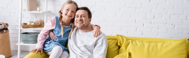 cheerful father and daughter hugging on couch at home, banner