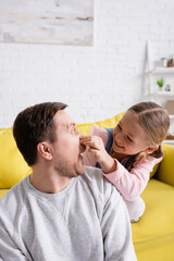 playful girl plugging nose of father while having fun in living room