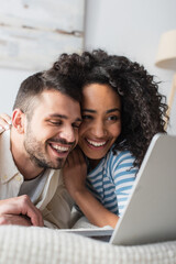 positive interracial couple chilling on bed and watching movie on laptop