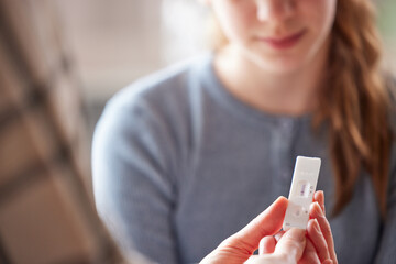 Mother And Daughter Looking At Positive Rapid Lateral Flow Test For Covid-19 On Daughter At Home