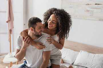 curly african american woman hugging positive boyfriend in bedroom