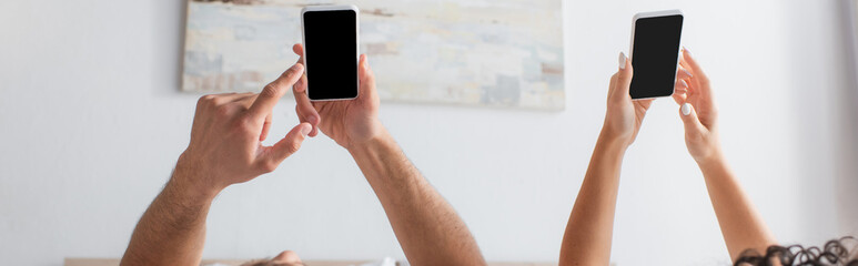 cropped view of multiethnic couple using smartphones with blank screen in bedroom, banner