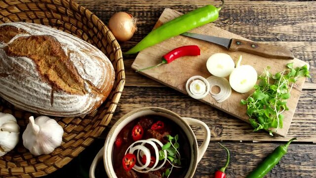 Traditional Hungarian beef goulash with garlic, bread and paprika, garnished with chopped onion and fresh marjoram.  4K UHD video, dolly side pan.