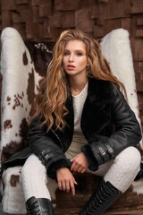 Young beautiful girl in white wool sporty knitten costume, black boots and leather puffer sitting...