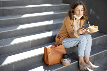 Pretty woman have outdoor lunch near office building while sitting on the stairs and using phone....