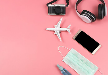 flat lay of airplane model, camera, headphones, mobile phone, protective face mask and alcohol spray  on pink background. Covid19 protection during traveling .