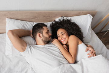 high angle view of bearded man looking at smiling african american girlfriend in bed