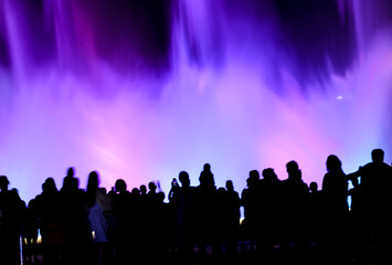 Silhouettes of people at a colored fountain at night.