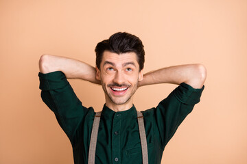 Photo of happy smiling cheerful handsome man hold hands head relaxing look copyspace isolated on beige color background