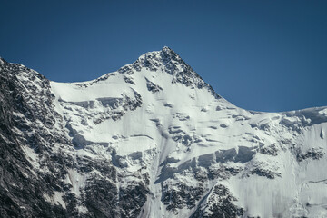 Awesome mountains landscape with black white snowy mountain top in sunny blue sky. Minimalist highland scenery with snow cornice on high mountain wall. Minimal view to wonderful snow-white pinnacle. © Daniil