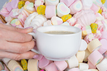Woman's hand with a cup of coffee on the background of marshmallows, close-up.Holiday concept, congratulations.