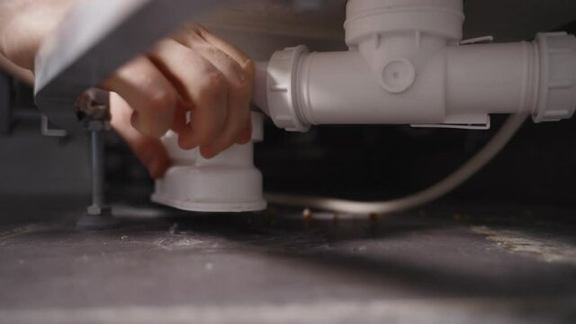 Plumber unscrewing bath trap. Close-up view.